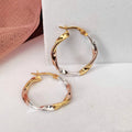 Gold hoop earrings on a white surface with a pink textured object in the background