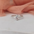 Silver ring with a pear-shaped diamond on a white surface with pink fabric in the background