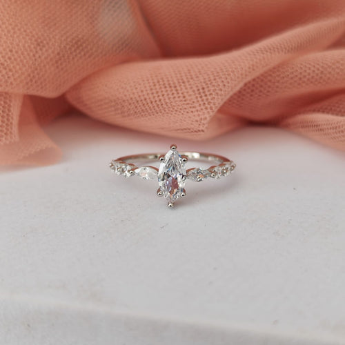 Silver ring with a pear-shaped diamond on a white surface with pink fabric in the background