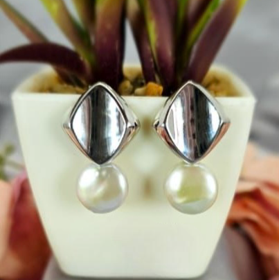 A pair of sterling silver drop earrings with pearls displayed on a white platform with a green plant in the background.