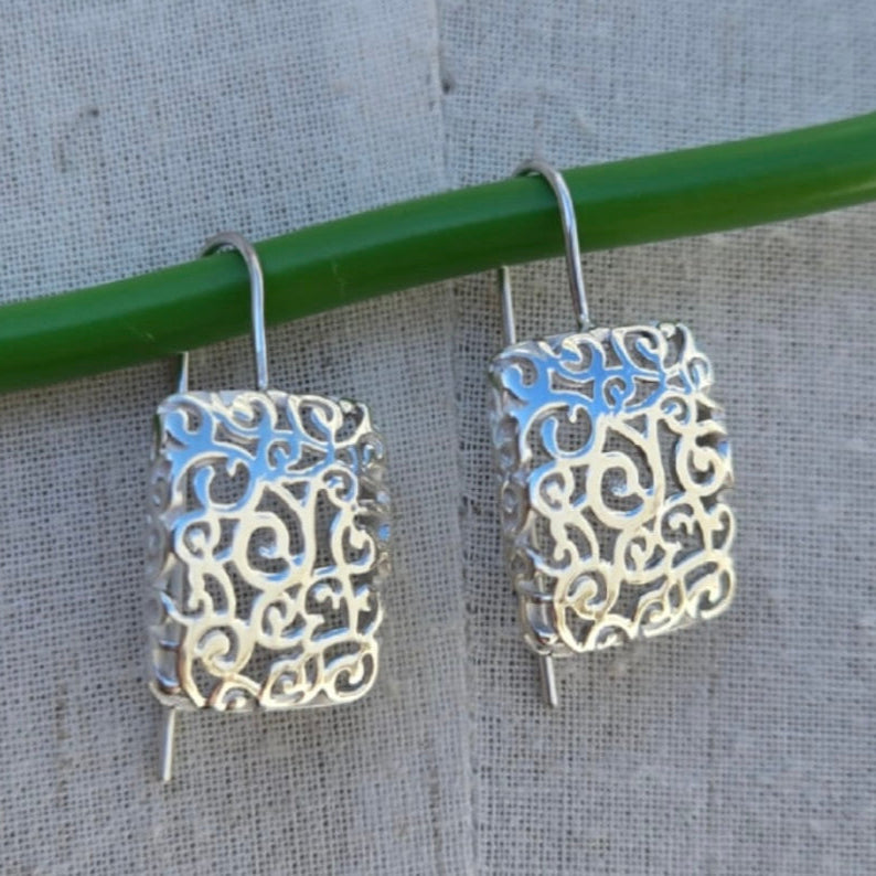 Silver filigree earrings hanging on a green rod against a gray background