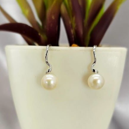 A pair of sterling silver earrings with a freshwater pearl drop design, displayed in a white vase with green leaves.