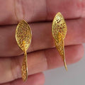Gold earrings held between fingers against a neutral background