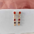 Pair of earrings with red and pink gemstones on a light gray background