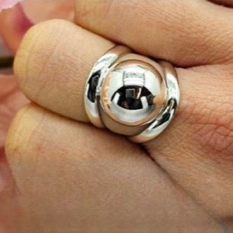 A sterling silver ball ring on a person's finger, with the ring's reflective surface clearly showing light and shadow.