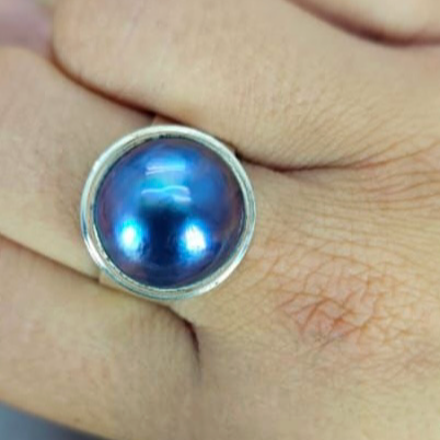 A blue Mabe pearl ring set in a silver band, displayed on a person's finger.