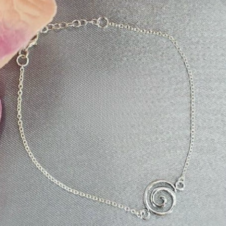 A sterling silver bracelet with a spiral design, displayed on a surface with a background of soft floral accents.