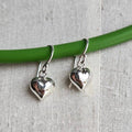 Silver heart-shaped earrings on a green wire against a gray fabric background