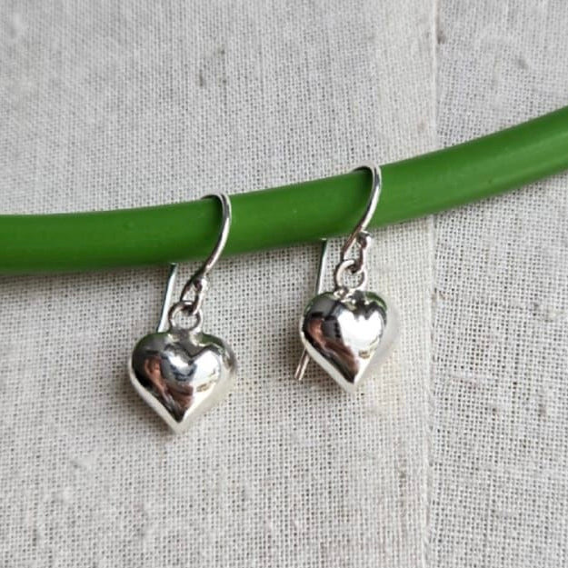 Silver heart-shaped earrings on a green wire against a gray fabric background