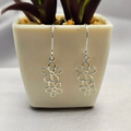 Sterling silver double daisy drop earrings displayed in a white vase with a green plant background.