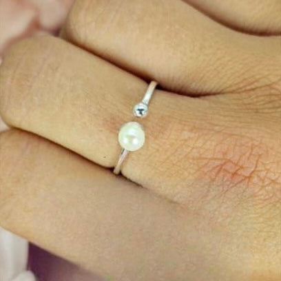 An adjustable sterling silver ring with a silver ball and a freshwater pearl on the end, displayed on a person's hand.