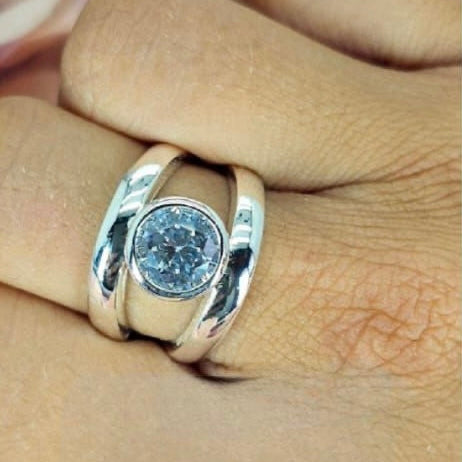 A silver ring with a large central cubic zirconia stone, displayed on a person's finger.
