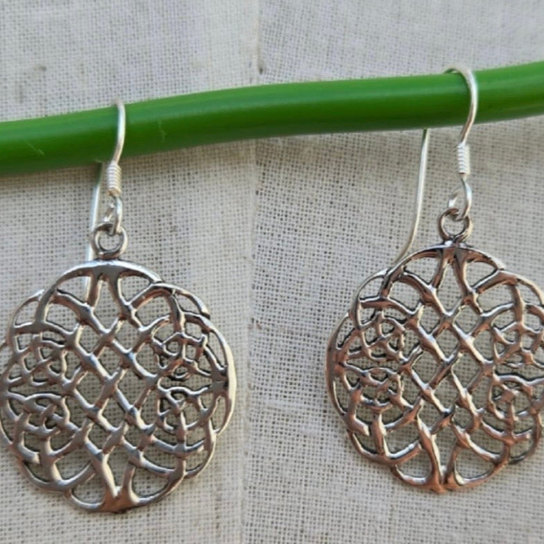 Silver filigree earrings hanging on a green rod against a beige fabric background
