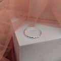 Silver ring on a white box with pink fabric in the background