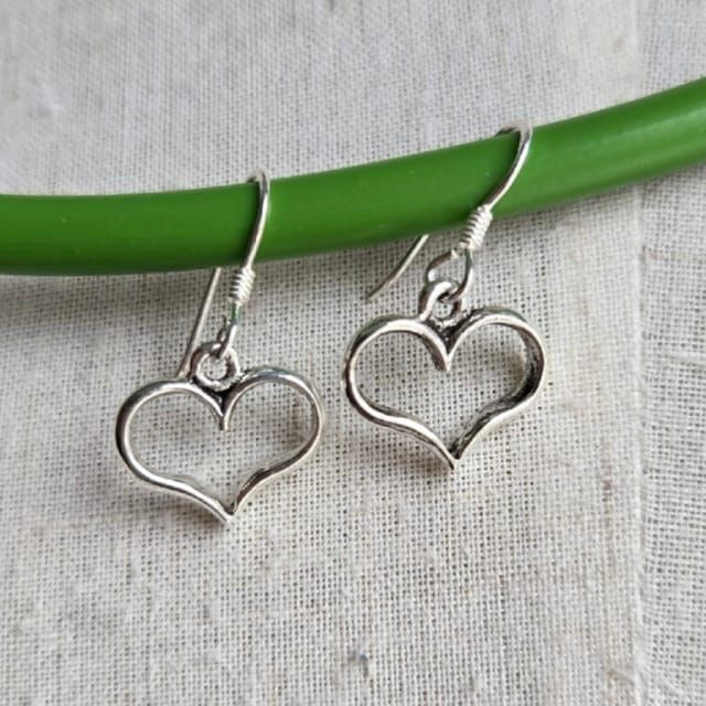 Silver heart-shaped earrings on a green stick against a gray background