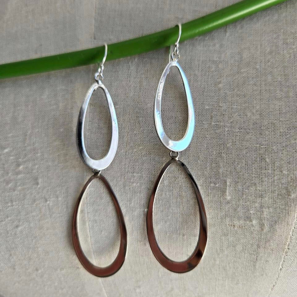 Pair of silver and bronze hoop earrings on a gray surface with a green stick.