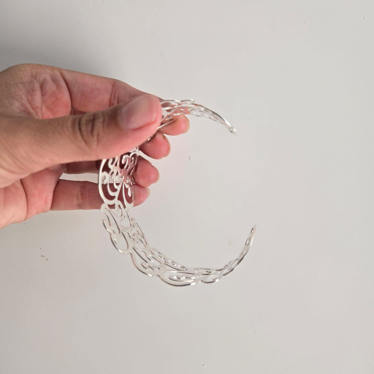 Hand holding a silver bracelet against a plain background