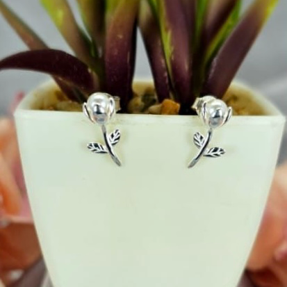A pair of silver stud earrings featuring a freshwater pearl centre, displayed in a white vase with green leaves.