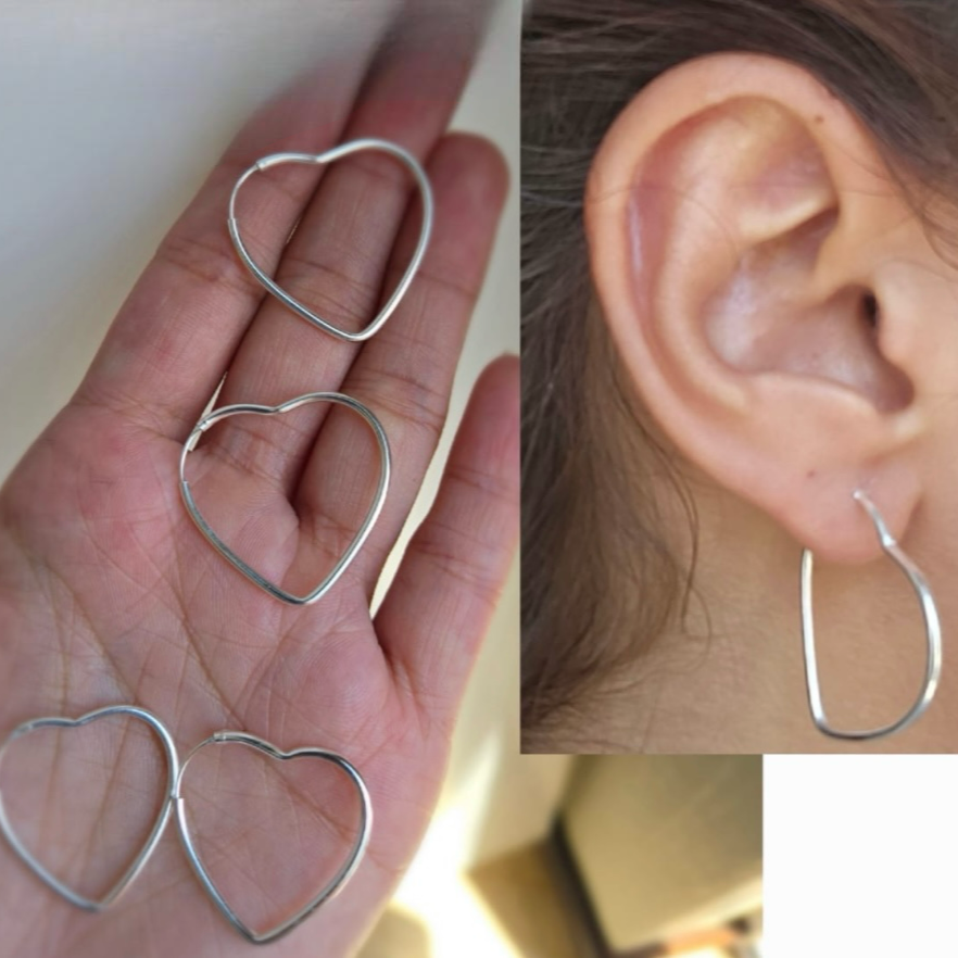 Handcrafted sterling silver heart-shaped hoops earrings displayed on a hand and worn on an ear.
