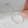 Silver hoop earrings on a light gray surface with a pink mesh fabric.