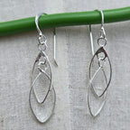 Silver earrings hanging from a green rod on a textured gray background