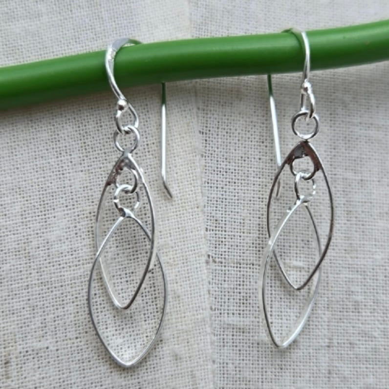 Silver earrings hanging from a green rod on a textured gray background