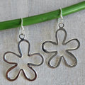 Silver flower-shaped earrings on a green stick against a gray background