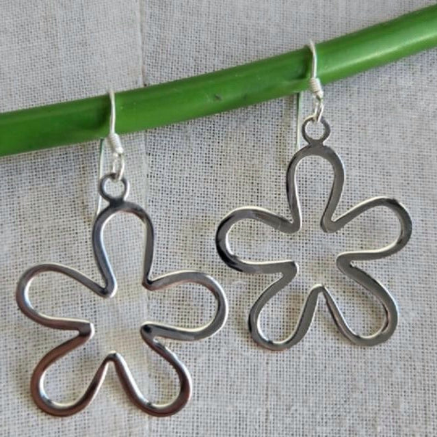 Silver flower-shaped earrings on a green stick against a gray background