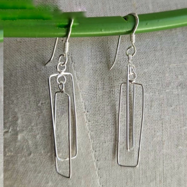 Silver earrings hanging from a green rod on a textured gray background