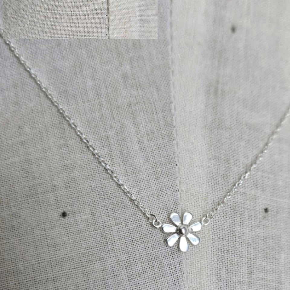 Silver necklace with a flower pendant on a gray fabric background