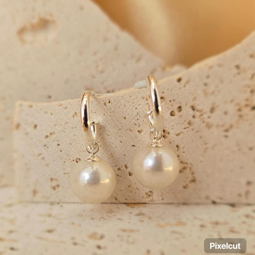 Pearl earrings with gold hooks on a textured beige surface