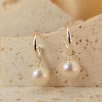 Pearl earrings with gold hooks on a textured beige surface