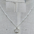Silver necklace with a flower pendant on a gray fabric background
