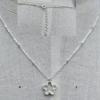 Silver necklace with a flower pendant on a gray fabric background