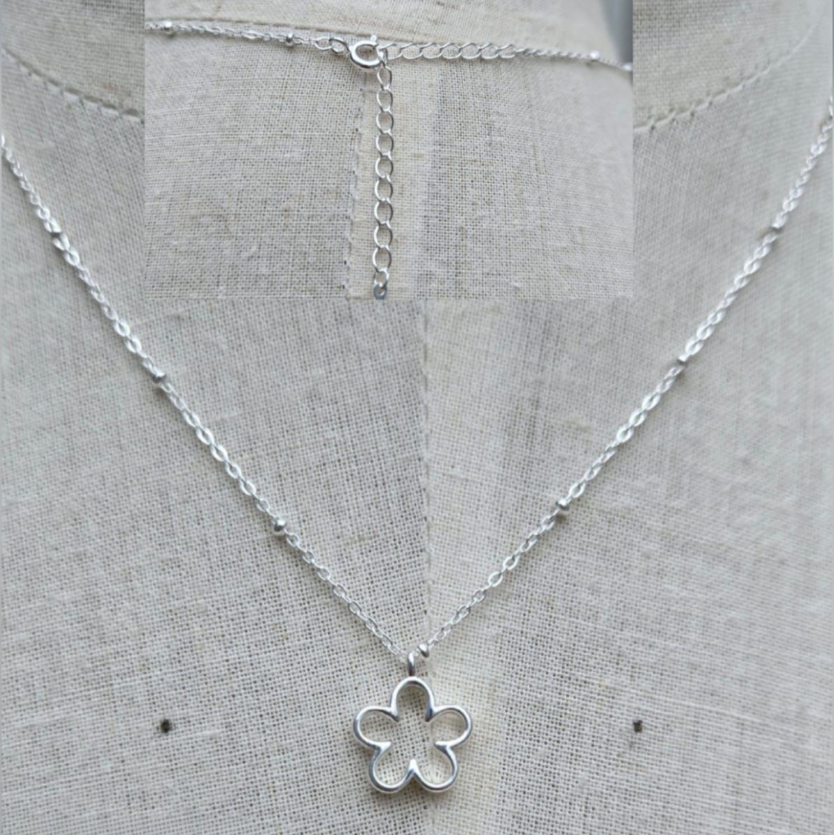 Silver necklace with a flower pendant on a gray fabric background