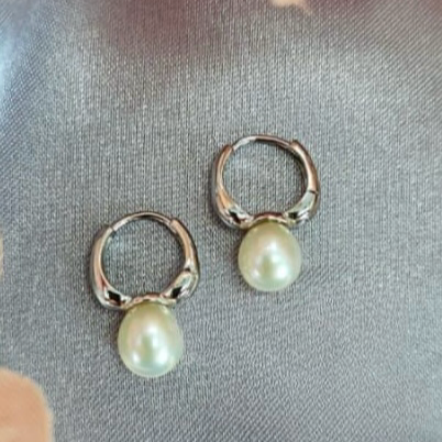 A pair of sterling silver hoop earrings with freshwater pearl drops on a grey fabric background.