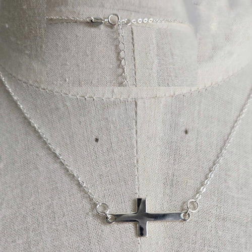 Silver necklace with a cross pendant on a light gray background
