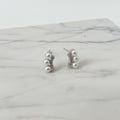 Pair of pearl earrings on a white stand with a pink lace background