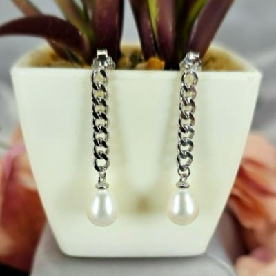 A sterling silver chain with freshwater pearls at the end, displayed in a white vase with a green plant in the background.