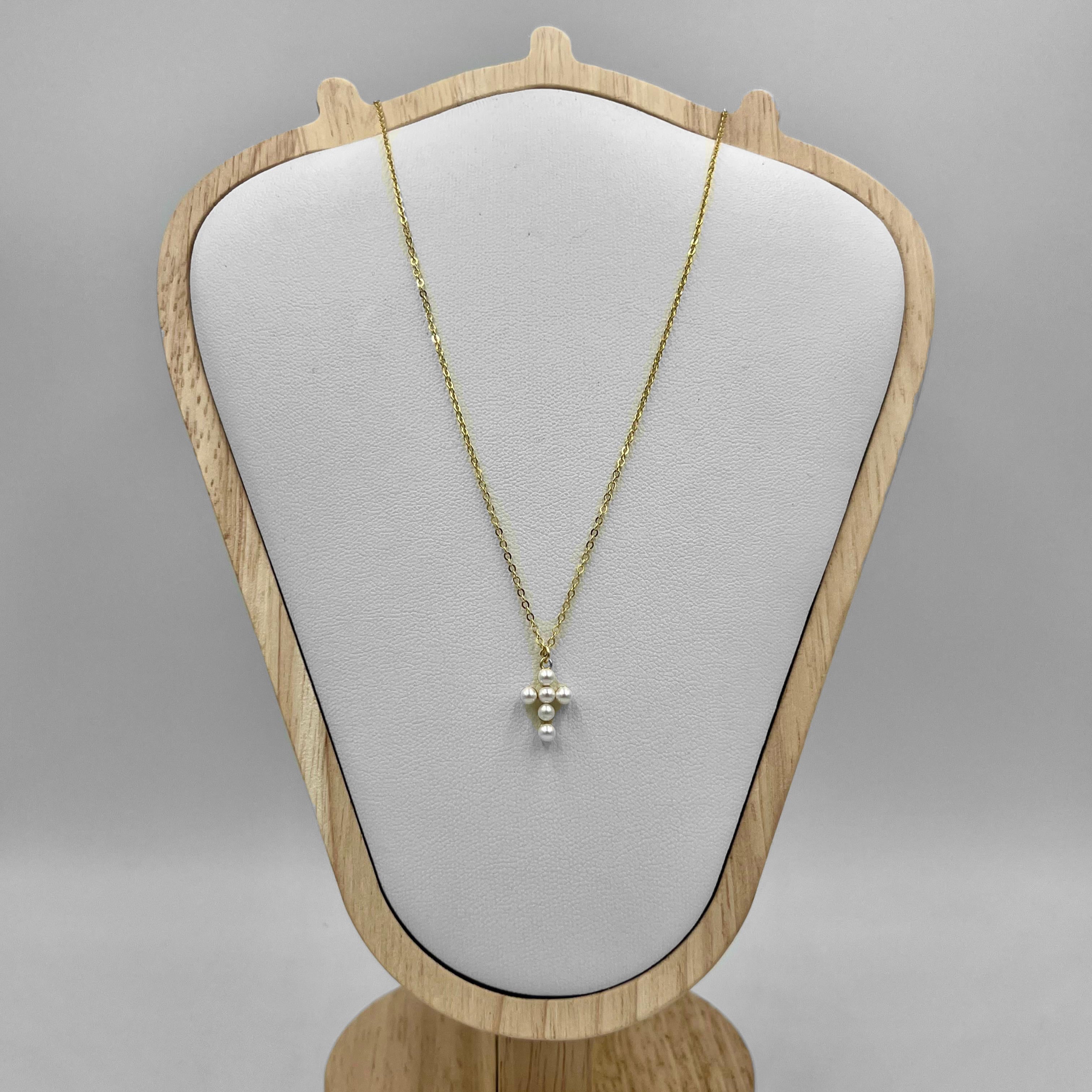 An 18c gold plated necklace with a sterling silver chain and a cross charm made of freshwater pearls, displayed on a wooden mannequin.