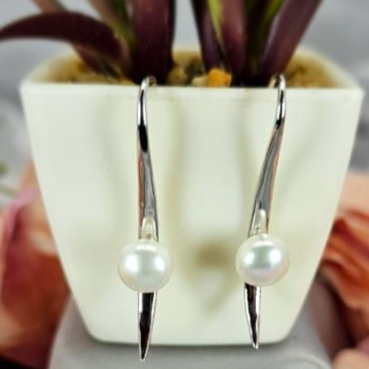 A pair of long straight look earrings with freshwater pearls, displayed on a plant pot.