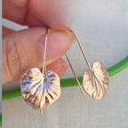 Gold leaf-shaped earrings held between fingers against a neutral background