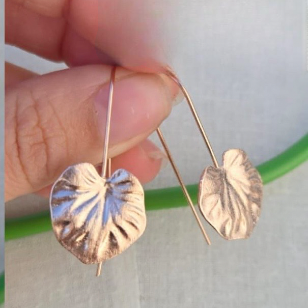 Gold leaf-shaped earrings held between fingers against a neutral background