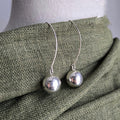 Silver sphere earrings on a mannequin with a green fabric background