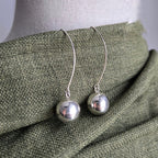 Silver sphere earrings on a mannequin with a green fabric background