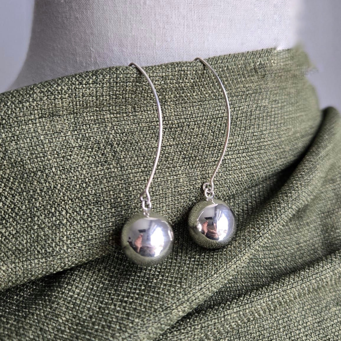Silver sphere earrings on a mannequin with a green fabric background