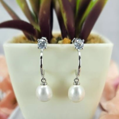 A pair of freshwater pearl earrings with cubic zirconia studs, displayed in a white vase with a green plant in the background.