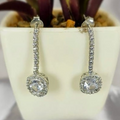 A pair of long drop earrings with cubic zirconia squares, displayed in a white vase with a green plant background.