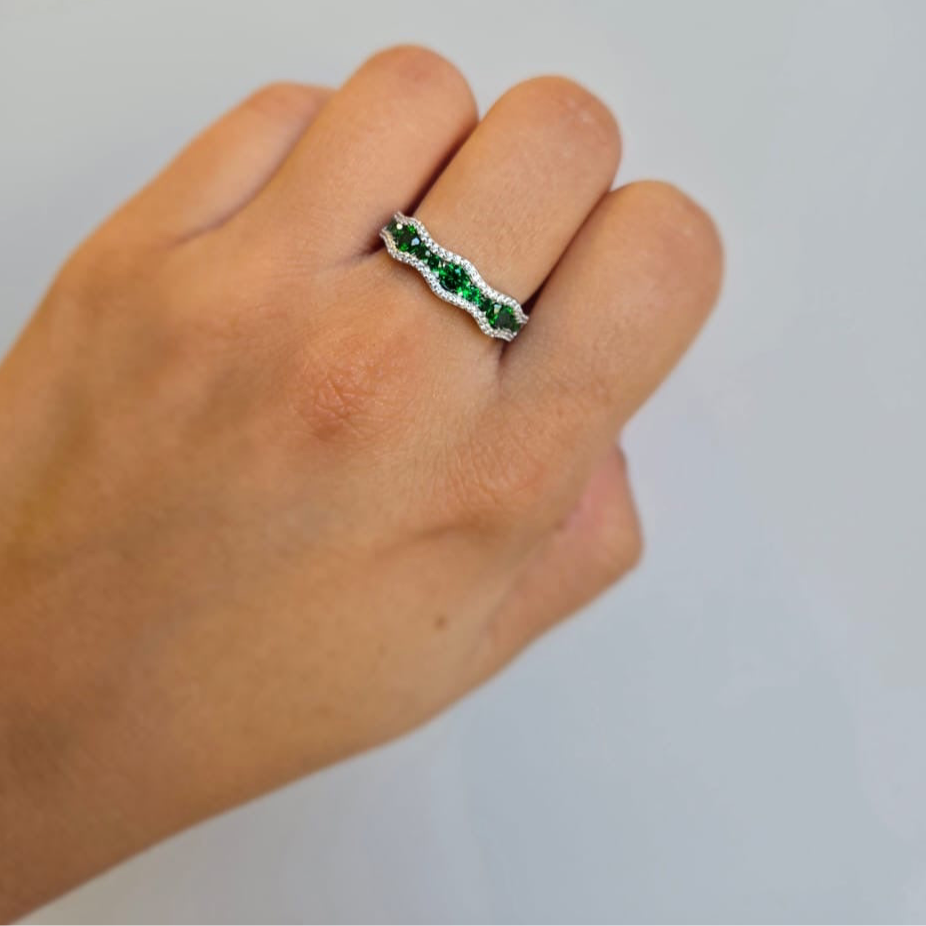 A hand wearing a green and clear stone pave ring with silver metal.