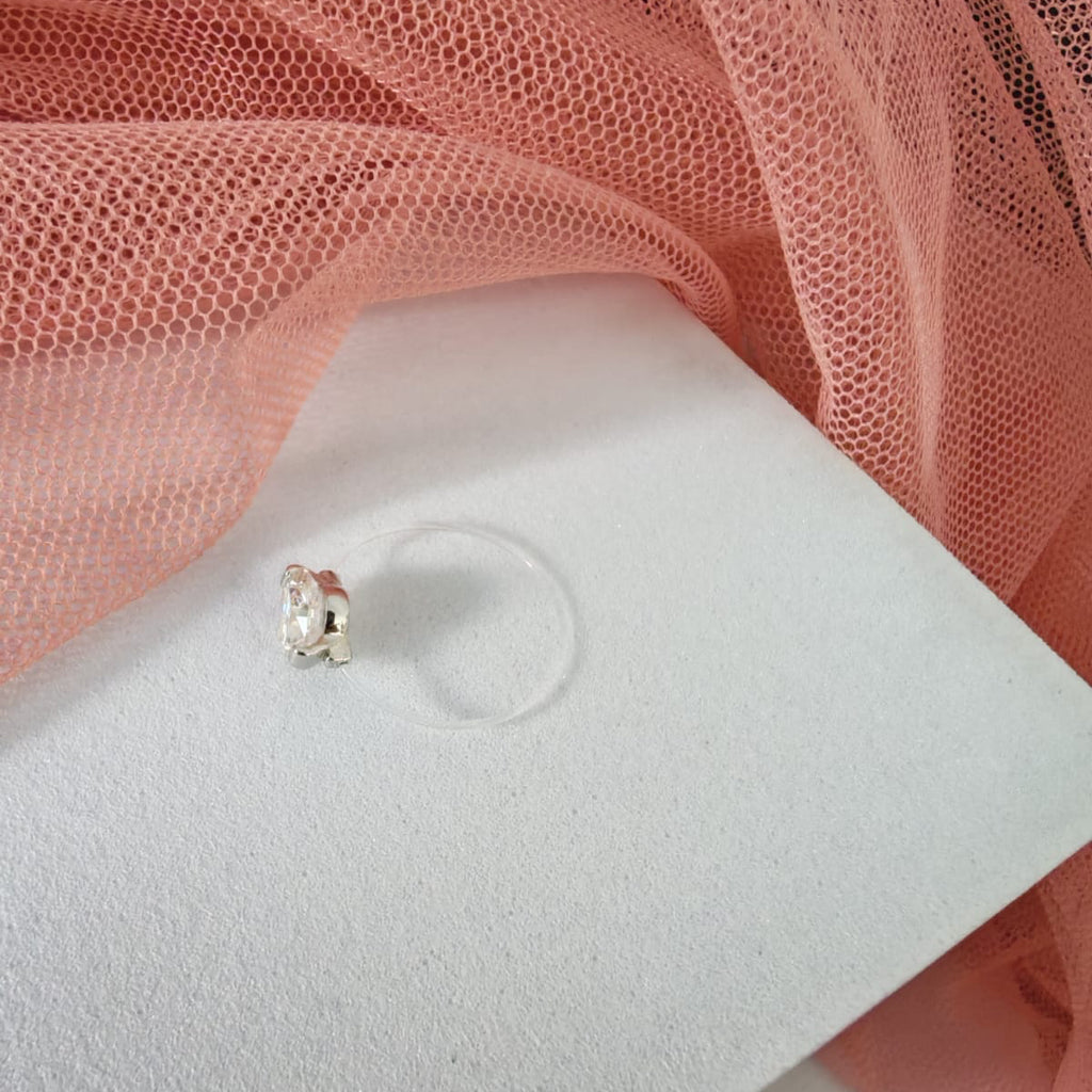 Silver earring on a white display card with pink fabric in the background
